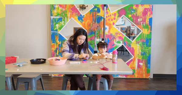 A woman and a child make art at a table in front of a colorful background.