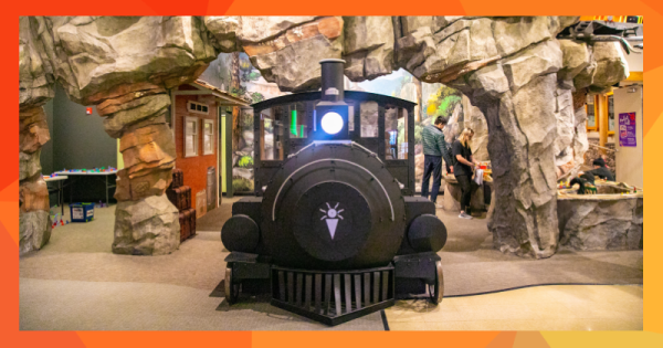 An interior scene at a children's museum with a large black train engine emerging from a mountain tunnel.