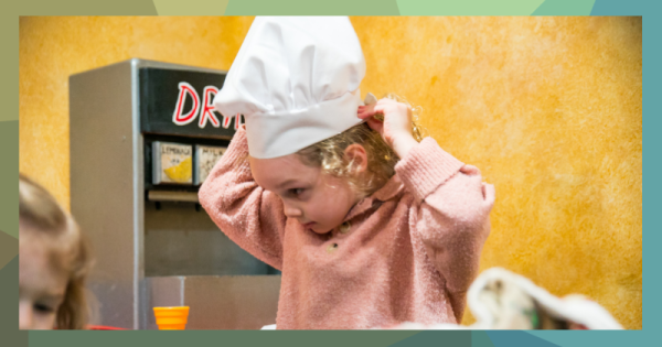 A little girl tries on a chef's hat.