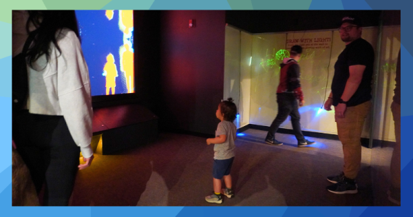 A toddler stands in a dark room looking at an illuminated screen.