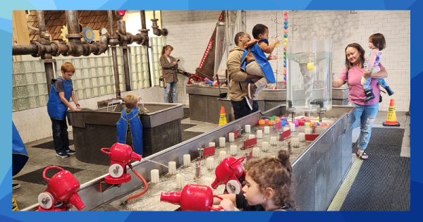 Young children are supported by adults as they play in an interactive water exhibit