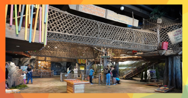 People playing in the interior of a children's museum, modeled on a woodland forest with rope bridges above.